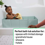 Baby in green Ingenuity Tuckaway Travel Tub in shower with yellow towel, compact and portable travel tub for kids aged 12-60 months.