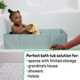 Baby in green Ingenuity Tuckaway Travel Tub in shower with yellow towel, compact and portable travel tub for kids aged 12-60 months.