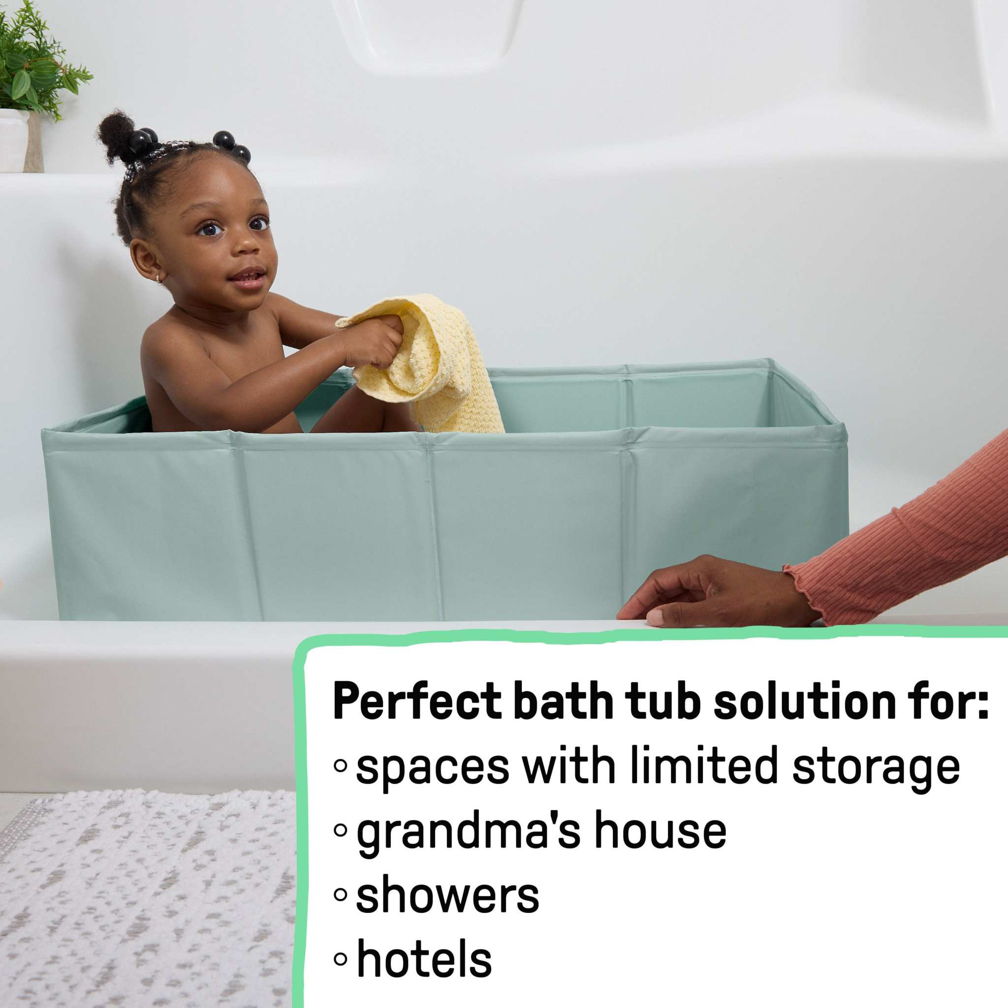 Baby in green Ingenuity Tuckaway Travel Tub in shower with yellow towel, compact and portable travel tub for kids aged 12-60 months.