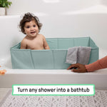 Baby sitting in a green Ingenuity Tuckaway Travel Tub placed inside a shower, converting it into a bathtub for kids up to 5 years old.