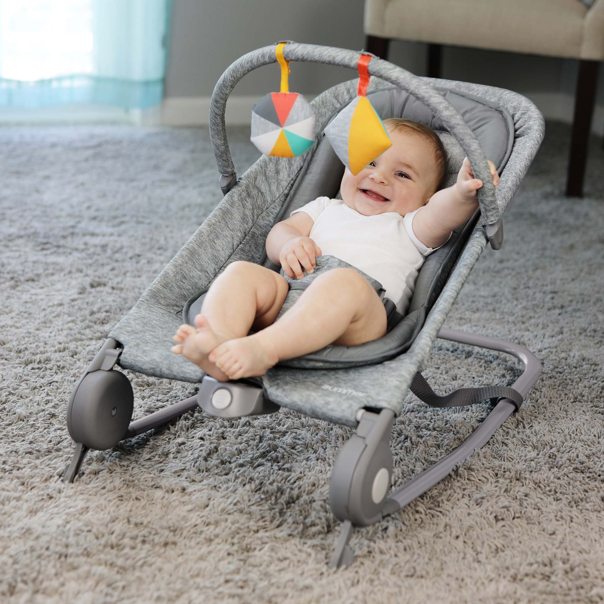Baby smiling in light gray tweed 2-in-1 Bouncer & Rocker with removable toy bar on carpet