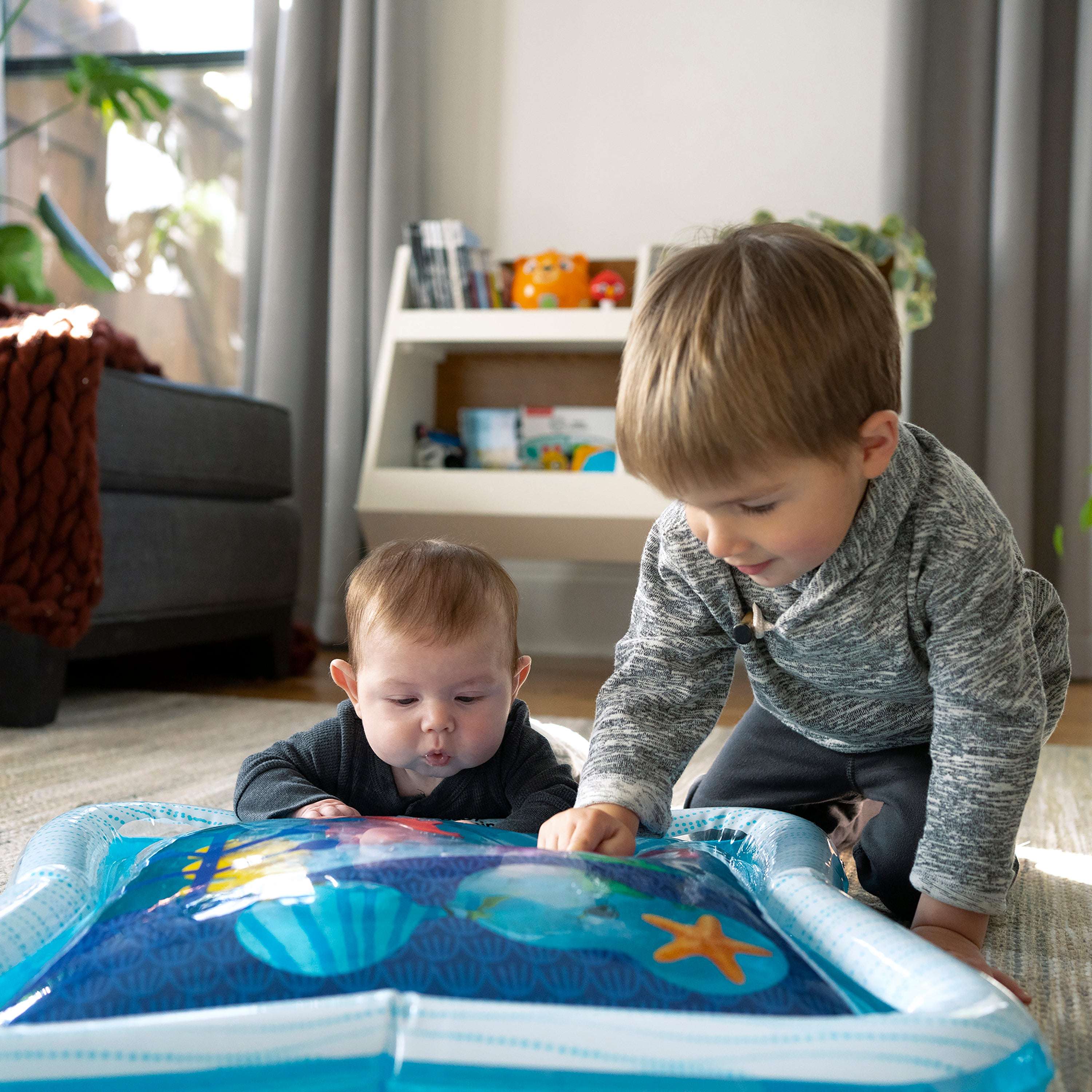 Baby and toddler playing with Baby Einstein Opus’s Ocean of Discovery™ Tummy Time Water Mat.
