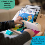 Baby Einstein Magic Touch Piano musical toy with child playing color-coded keys, featuring three modes of play and colorful music sheets.