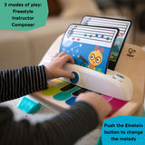 Baby Einstein Magic Touch Piano musical toy with child playing color-coded keys, featuring three modes of play and colorful music sheets.