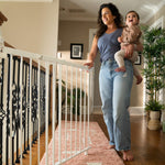 White metal safety gate installed at the top of stairs, woman holding a child, open door feature.