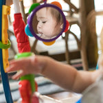 Baby enjoying the Baby Einstein Neighborhood Symphony Activity Jumper with colorful toys and a mirror.