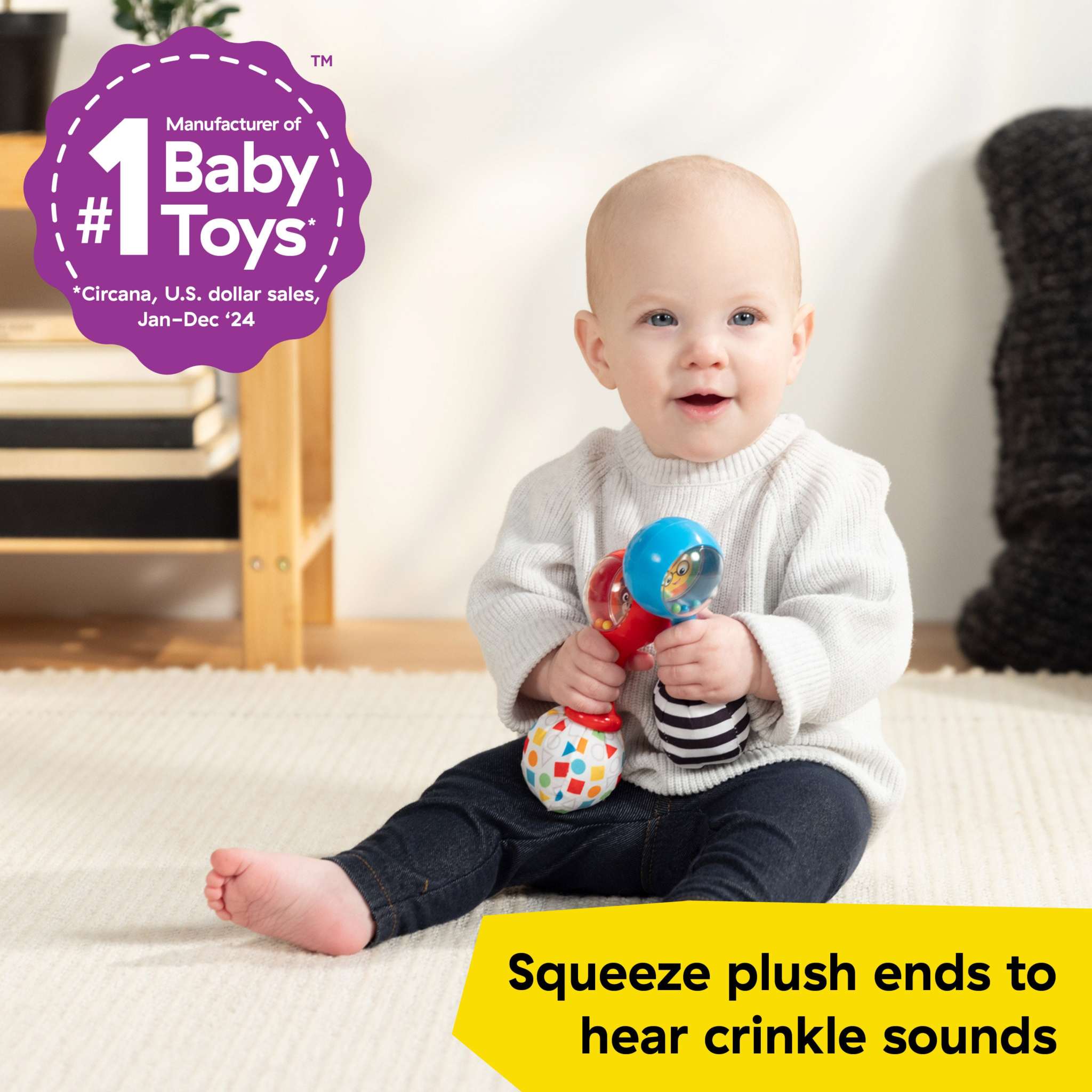 Baby holding Baby Einstein First Tunes plush maracas with crinkle sounds, sitting on floor.