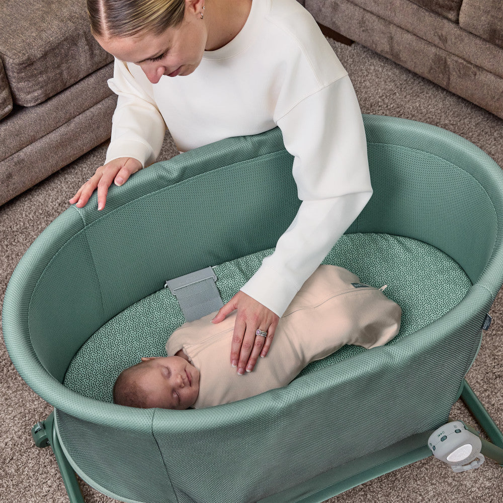 Woman interacting with a baby in a green bassinet.
