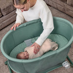 Woman interacting with a baby in a green bassinet.