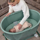 Woman interacting with a baby in a green bassinet.