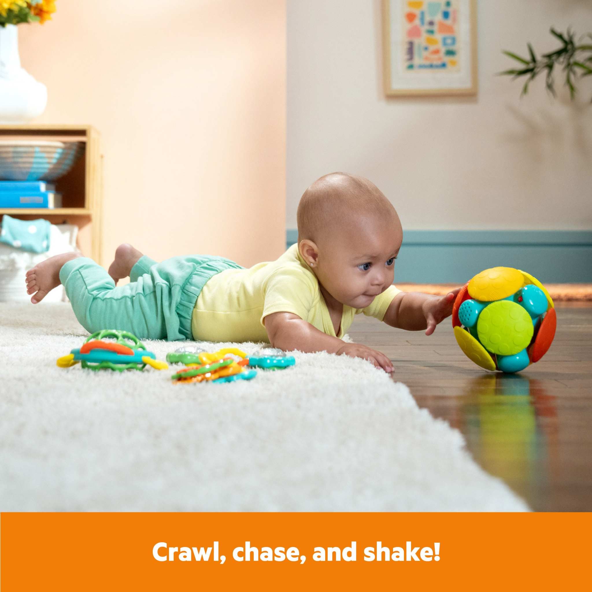 Baby crawling and reaching for colorful Bright Starts Catch Me Smile gift set toy ball on floor with teething toys nearby