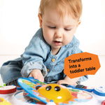 Baby playing with the Discovering Music Activity Table featuring piano, drum, guitar, and French horn instruments