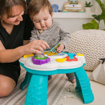 Baby playing with Discovering Music Activity Table featuring piano, guitar, drum, and French horn instruments