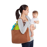 Mother carrying baby with a brown bag holding the Door Jumper, showcasing portability and convenience.